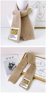 Detail of beige knit scarf showing wavy texture and Good Luck square letter patch