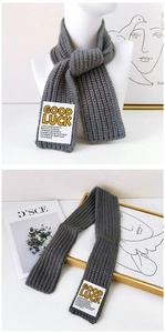 Detail of gray ribbed knit scarf featuring a white Good Luck message woven patch