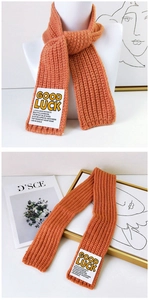 Detail of orange knitted scarf with GOOD LUCK label and thick vertical ribbed texture