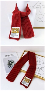 Close-up of red knit scarf with Good Luck patch and white label detail for winter