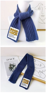 Detail of blue ribbed knit scarf featuring a white Good Luck woven label patch