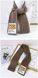 Close-up of GOOD LUCK patch on coffee brown chunky knit scarf with vertical stripes