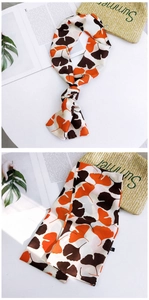 Detail of long silk-like scarf featuring orange and brown ginkgo leaf pattern prints
