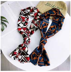 Detail of geometric print twilly silk scarves on white surface with summer straw hat
