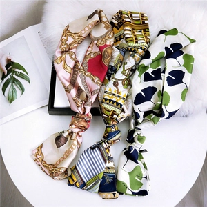Three elegant narrow silk scarves featuring equestrian and floral prints on a white table