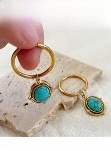 Close-up of golden oval stainless steel earrings with inlaid turquoise stone detail