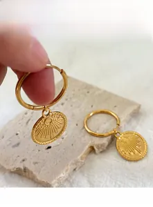 Detail of 18K gold-plated stainless steel hoop earrings with sunburst charms on stone background