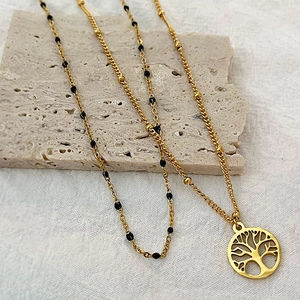 Collana Albero della Vita placcata oro con perline nere su fondo in pietra minimale