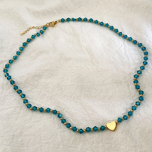 Collier en perles de cristal bleu avec pendentif coeur plaqué or 18 carats sur lin blanc