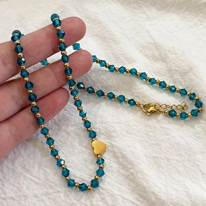 Collier ras de cou perlé vert avec pendentif cœur plaqué or 18 carats tenu en main