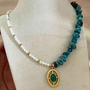Irregular natural stones and pearl necklace with a gold oval pendant on a display bust