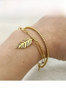 Detailed view of layered 18K gold-plated leaf charm bracelet on a wrist