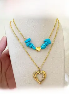 Detail view of a double-layer gold necklace featuring turquoise beads and double heart charms