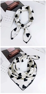 Détails d'un foulard en soie crème avec imprimé cœurs noirs et bordure élégante