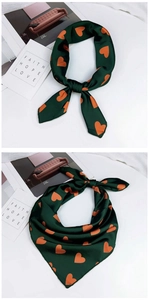 Détail d'un foulard en satin vert foncé à motifs cœurs orange noué en tour de cou