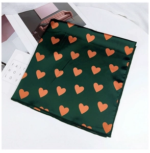 Détail d'un foulard carré en satin vert foncé avec cœurs orange et coutures de qualité