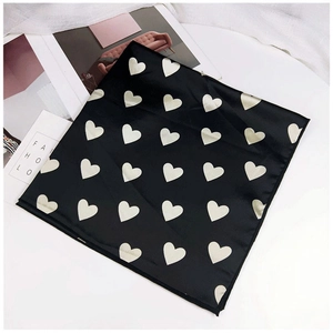 Vue à plat d'un foulard en soie noir à motifs cœurs dorés avec magazine de mode