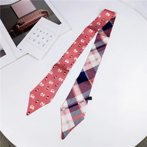 Detailed view of skinny scarf with pink cartoon cat pattern and plaid design on white table