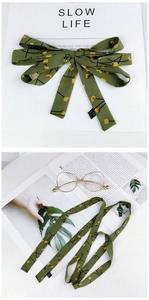 Close-up of green floral skinny scarf tied as a bow with 100% polyester wash label