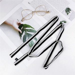 Narrow black and white striped silk scarf tied on a bag with minimalist lifestyle props