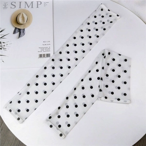 Detail of white mesh sun protection sleeves with retro black polka dots on white table