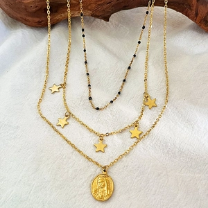 Collier multi-rangs doré vintage avec médaille Marie et étoiles sur un fond en bois sombre