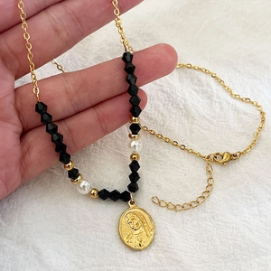 Vista a mano di una delicata collana d'oro con perline nere e ciondolo a medaglia
