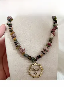 Détail d'un collier de pierres naturelles colorées avec pendentif médaillon soleil doré