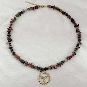 Collier en pierres naturelles colorées avec pendentif soleil doré sur fond de tissu blanc