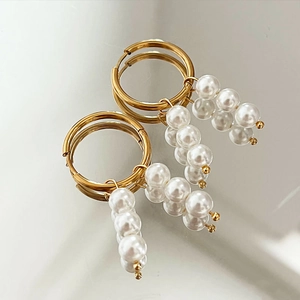 Elegant gold hoop earrings with white pearl cluster drops on a reflective surface