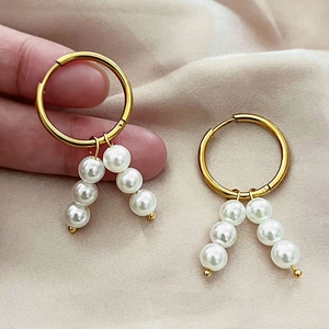 Minimalist gold hoop earrings with hanging white pearls on a soft pink satin backdrop