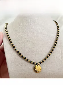 Gros plan du collier perlé fait main or et noir avec pendentif floral rond gravé