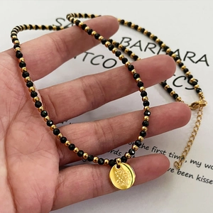 Collier artisanal de perles noires et dorées avec un pendentif rond à motif floral