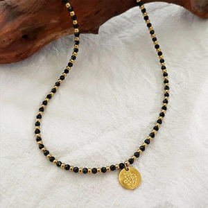 Collier artisanal perlé avec pierres noires et pendentif doré gravé de fleurs