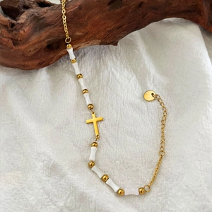 Beaded gold cross bracelet with white bamboo-style tubes and adjustable chain on wood