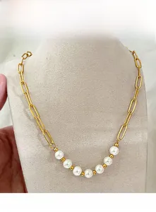 Détail d'un collier chaîne trombone dorée avec sept perles blanches et accents dorés