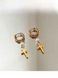 Détail de boucles d'oreilles créoles dorées 18k en acier avec perle blanche et croix