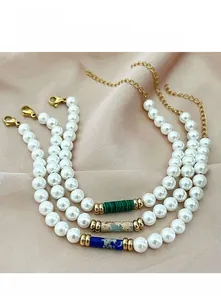 Three beaded pearl necklaces with green, blue, and brown stone cylinders on pink fabric