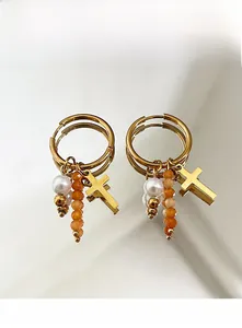 Détail de créoles dorées avec pendentif croix, perles et perles à facettes orange