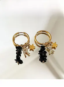 Macro detail of 18k gold earrings with star, natural stone, and crystal letter charms