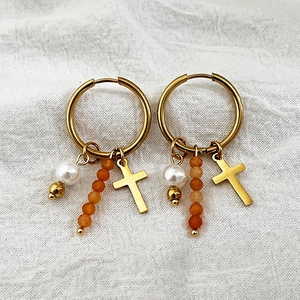 Créoles dorées avec perle, perles orange et pendentifs croix sur tissu en lin blanc