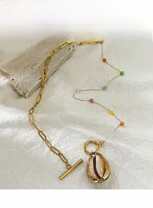Detailed close-up of gold paperclip chain necklace with shell pendant and colorful beads