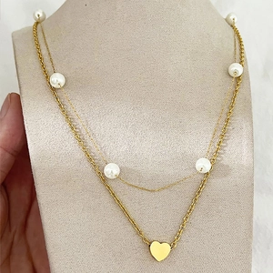 Collier double rang doré avec perles et pendentif cœur sur un buste beige