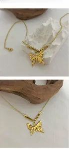 Nahaufnahme der goldenen Schmetterlingskette mit Perlen auf minimalistischem Grund
