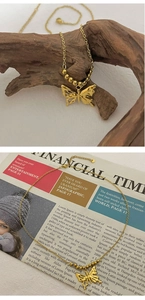 Detailansicht einer goldenen Schmetterlingskette mit Perlenkette auf rustikalem Holz