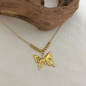 Elegante goldene Schmetterlingskette mit Perlenkette auf natürlichem Holzdisplay