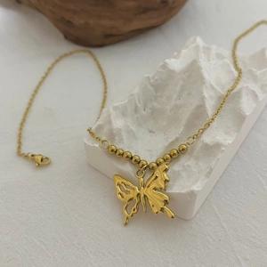 Goldene Halskette aus Edelstahl mit Schmetterlingsanhänger auf einem Bergsockel