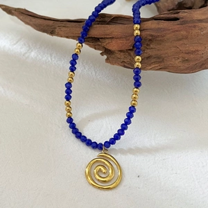 Handmade beaded necklace with blue stones and a gold spiral pendant on driftwood