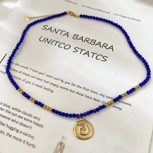 Vintage blue faceted bead necklace with gold spiral pendant on a minimalist art card
