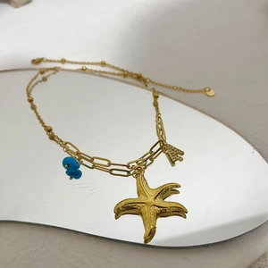 Collier étoile de mer doré avec perle bleue et lettre A sur une surface en miroir